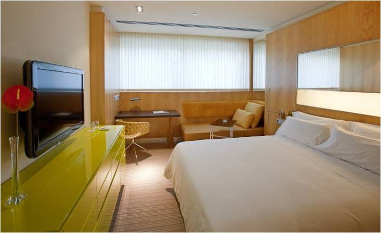 Habitación moderna del Hotel Alfonso Zaragoza con cama doble, muebles de madera y zona de estar junto a la ventana.