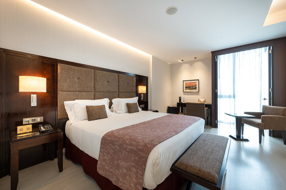 Habitación elegante del Hotel Plaza Diagonal Zaragoza con cama doble, iluminación cálida y zona de estar junto a la ventana.