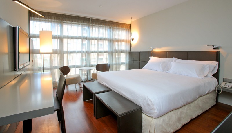 Habitación moderna del Hotel Reina Petronila Zaragoza con cama doble, escritorio y ventanal amplio.